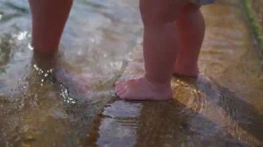 Sığ göl suyunda küçük çocukların ayaklarının yakın çekimi, küçük bir çocuk sıcak yaz aile günü boyunca ayak parmaklarının etrafında hafif dalgalanmalarla taş basamaklarda duruyor.