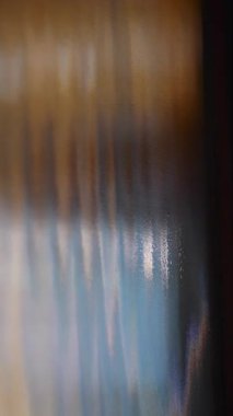 Mavi ve kehribar tonlarına sahip soyut cam yüzey, yumuşak yayılmış röfleler ve rüya gibi yansımalar, yaratıcı projeler için sanatsal makro arkaplan