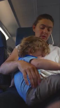 Yolculuk sırasında kucağında bebek taşıyan bir anne, aşağıya bakarken çocuğu rahatlatıyor, yakın ebeveynlik zamanı yolculuk sırasında bağ ve özen gösteriyor.