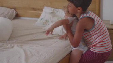 Çocuk oyuncağını neşeyle kaldırıyor ve yatağa atıyor. Neşeli bir an. Evde eğlenceli vakit geçirirken kahkaha, enerji ve kardeşçe bağ kuruyor.