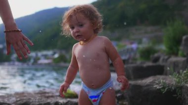 Bez ve kehribar kolye takmış, su kenarındaki taş basamaklarda çıplak ayakla duran çocuk, yeşil ve kayalıklarla çevrili eğlenceli bir yaz gününün tadını çıkarıyor.