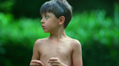 Kapalı çekimde elinde küçük çiçekler olan genç bir çocuk odaklanmış bir ifadeyle aşağıya bakıyor. Huzurlu bir yaz parkı anı. Merakını ve yoğunluğunu gösteriyor.