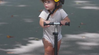 Skuter gidonu tutan, sarı kask takan, meraklı bir bebeğin açık havayı keşfederken, erken çocukluk gelişimi ve oyuncu öğrenme sürecinde yan yana baktığı yakın plan.