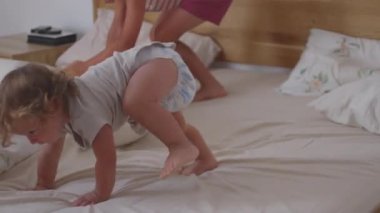 Küçük çocuk yatakta emekliyor ve neşeli bir anda yere kayıyor, evde merak, hareket ve kaygısız keşifler gösteren enerjik kapalı mekan aktivitesi