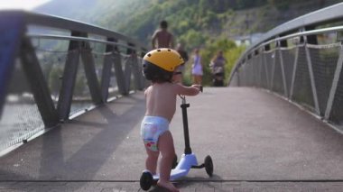 Yürüyen bir çocuk yaya köprüsünde yürürken sarı kask takar, çevreyi dikkatle ve kararlılıkla keşfeder.