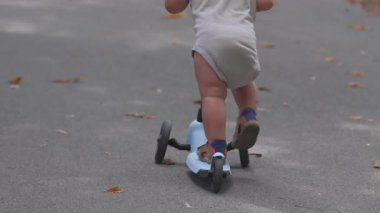 Küçük çocuk park yolunda motosikletle uzaklaşıyor, küçük bir çocuğun dışarıda özgürlüğün tadını çıkarışının dikiz görüntüsü, erken çocukluk macerası, neşeli bir keşif ve doğa hareketi.