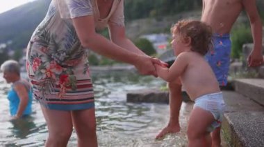 Göl kenarında annelere tutunan küçük bir çocuk, taş basamakların yanında dururken sıkıca tutulan küçük bir çocuk, açık havada ailesiyle duygusal bir yaz anı.