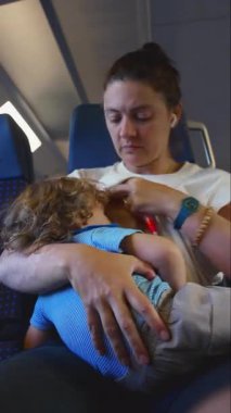 Anne, çocuğunu tren koltuğunda emzirirken çocuğu rahatlatırken, samimi ebeveynlik anlarında bağ, şefkat ve özen gösterir.