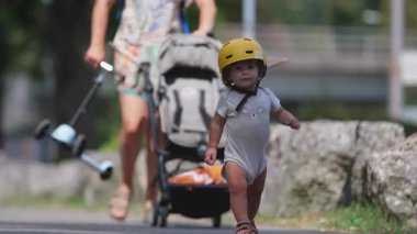 Sarı kask takan, bebek arabasının yanında yürüyen gülümseyen çocuğun yakın çekimi. Neşeli bebek. Ailecek parkta geçirdiğimiz yaz tatilinin tadını çıkartıyor.