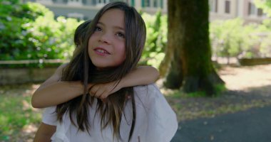 Kız kardeşi, güneşli bir günde erkek kardeşini sırtında taşıyor. Hem gülüyor, hem de bahçenin tadını çıkarıyor. Etrafı yeşillik ve gölgeli yürüyüş yolu ile çevrili.