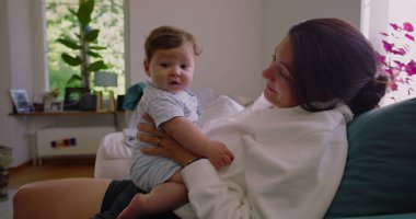 Anne, güneşli bir oturma odasında bebeğine gülümserken anne ve çocuk SD 480p arasında sıcak ve sevgi dolu bir bağ kuruyor.