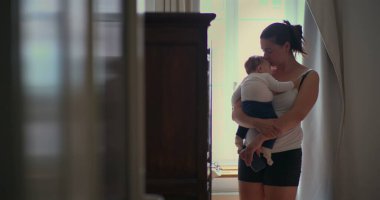 Anne bebeğini sevgi dolu bir şekilde kucağında tutarak hafifçe aydınlatılmış bir odada yürüyor, huzurlu bir bağlantı anı yaratıyor ve SD 480p 'lik sıcak bir evde bakıcılık yapıyor.