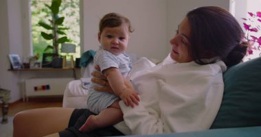 Anne, güneşli bir oturma odasında bebeğine gülümserken anne ve çocuk SD 480p arasında sıcak ve sevgi dolu bir bağ kuruyor.