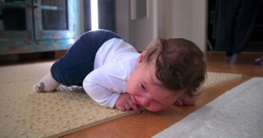 Ağlayan bebek yerde yatıyor, sıkıntı ve rahatsızlık gösteriyor, ev ortamında yumuşak bir paspas üzerinde duygularını ifade ediyor, erken gelişim zorluklarını ve hislerini vurguluyor.