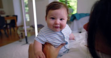 Bebeğin doğrudan kameraya baktığı yakın çekim. Bu sırada anne, bebeği sevgi dolu bir şekilde sakin bir evde tutarak anne-baba ve çocuk arasındaki huzurlu ve samimi sahneyi yakalıyor.