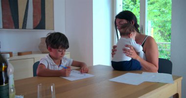 Çocuk, anne yanında bebeği tutarken evde eğitim işine odaklanmış, aile desteğini göstermiş ve sakin bir evde eğitim ve büyüme ortamı sağlamıştır.