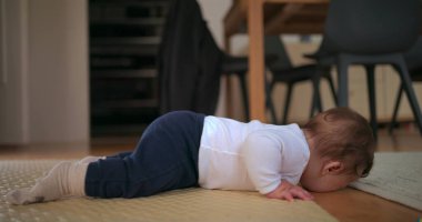 Bebek yüzüstü yatar, kafası hayal kırıklığına uğrar, huzurlu bir ev ortamında yumuşak bir paspas üzerinde emekleme girişiminde bulunurken duygularını ifade eder.