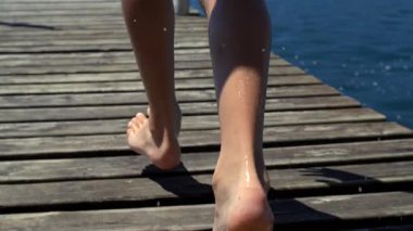 Islak ayaklı çocuğun rıhtımda koşuşunun yakın çekimi, yavaş çekim videosu neşeli bir yaz havası, kaygısız enerji ve suya doğru neşeli bir açık hava hareketi yakalıyor.