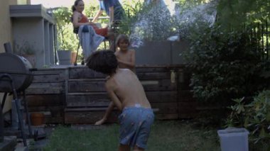 İki üstsüz çocuk yaz günü bahçede su savaşı yapıyor. Aile terasta dinlenirken su sıçratıyorlar. Yavaş çekimde çocukluk anılarının tadını çıkarıyorlar.