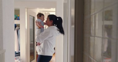 Anne koridorda bebeğini yüzüne yakın kaldırıyor, doğal ışık, sıcak ve sevgi dolu aile anı, samimi otantik yaşam tarzı, beslenme ve bağ kurma sahnesi.