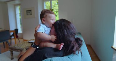 Anne ve bebek, parlak bir oturma odasında birlikte oynuyorlar. Neşeli anlar, kahkahalar ve doğal ışıklandırmayla bağ kuruyorlar.