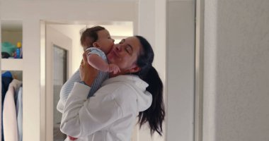 Anne koridorda bebeğini yüzüne yakın kaldırıyor, doğal ışık, sıcak ve sevgi dolu aile anı, samimi otantik yaşam tarzı, beslenme ve bağ kurma sahnesi.