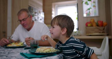Baba ve oğul aile yemeği sırasında masada birlikte yemek yiyorlar, özgün bir bağ sergiliyorlar ve rahat bir yuva ortamında günlük aile hayatı sergiliyorlar.