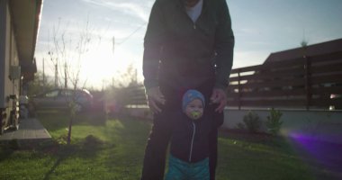 Baba, çocuğun aile evinin yakınındaki çimenlikte yürümesine yardım ediyor. Çocuğun hareketini ve dengesini destekliyor. Bağlanmayı ve sevgiyi teşvik ediyor.