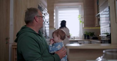 Baba bebeğini kucağında tutarken anne mutfakta hazırlanıyor sıcak ve sevgi dolu bir aile ortamında ev ortamında.