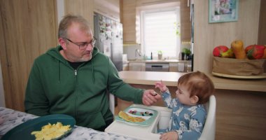 Baba, ufaklığın renkli kahvaltı tabağını meyve ve gözlemelerle keşfetmesine yardım ediyor.
