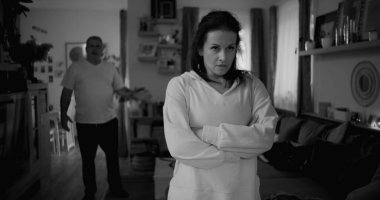 Şiddetli tartışmalar sırasında sert ifadeli bir kadının yakın çekimi, arka planda bulanık bir adam öfkeyle işaret ediyor, duygusal gerilimi yakalıyor ve çözülmemiş çatışmaları yakalıyor.