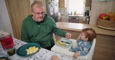 Baba, ufaklığın renkli kahvaltı tabağını meyve ve gözlemelerle keşfetmesine yardım ediyor.