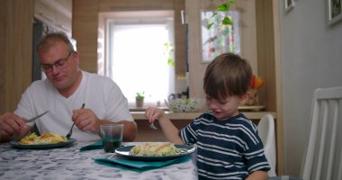 Aile masada bir yemeği paylaşır, anne bulaşıkları servis ederken baba ve oğul doğal sohbetler yapar, bağlantıyı ve sıcaklığı ön plana çıkarır.