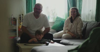 Anne ve baba kanepede oturup çocuğa gülümsüyor kahve masasında oyuncak trenle oynuyor rahat oturma odası düzeninde, neşeli aile anları, kapalı alanda kaynaşma zamanı.