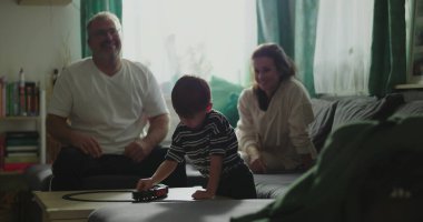 Anne ve baba kanepede oturup çocuğa gülümsüyor kahve masasında oyuncak trenle oynuyor rahat oturma odası düzeninde, neşeli aile anları, kapalı alanda kaynaşma zamanı.