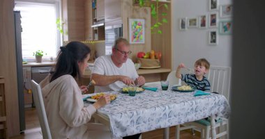 Aile yemek masasında birlikte yemek yiyor, anne babalar çocukla yemek yiyor, aile bağlarını güçlendirme anı paylaşılan yemeğe ve sohbete odaklanıyor.