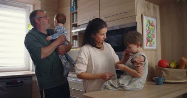 Modern mutfaktaki aile etkileşimi, baba bebeğini kucağında tutarken annesinin tezgahta oturması, sıcak aile bağlarının kurulması.