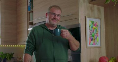 Sıcak içeceğe, kahveye ya da çaya tepki veren bir adam. Düşünce anı, gündelik mutfak düzeni, modern iç mekan, ev içi aktiviteler, evde kişisel zaman geçirme.