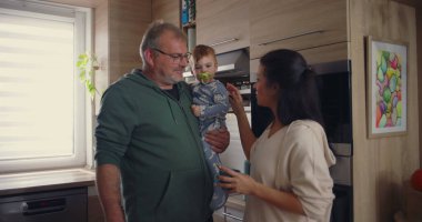 Anne, modern mutfakta babamla konuşurken bebeğin kafasına şefkatle dokunuyor. Günlük ev ortamında sıcak aile etkileşimi..