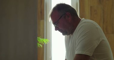 Banyo aynasının önünde düşünceli bir şekilde oturan adam, sakin bir ifadeyle yan profil görüntüsü, sessiz ve huzurlu iç mekan ortamını yansıtıyor.