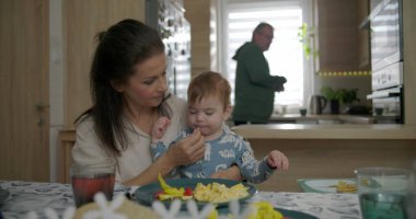 Anne kahvaltı masasında bebeği besliyor, bebekle kaynaşıyor çırpılmış yumurta ve sebzeleri keşfediyor, sıcak mutfak ortamında aile bağlarını besliyor.