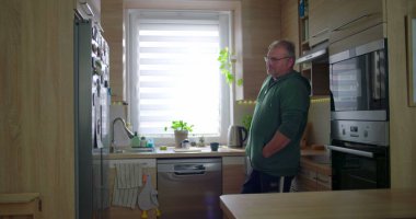 Modern mutfakta duran adam, düşünceli poz, gündelik yaşam tarzı, elleri cepte, huzurlu ev düzeni, doğal ışık ile ev rutini