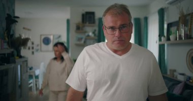 Erkek, tartışma sırasında yoğun bir ifadeyle kameraya bakıyor, kadın oturma odasında, gergin ve duygusal bir ilişki çatışması ve hüsran anı yaşıyor.