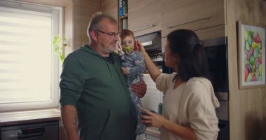 Anne, modern mutfakta babamla konuşurken bebeğin kafasına şefkatle dokunuyor. Günlük ev ortamında sıcak aile etkileşimi..