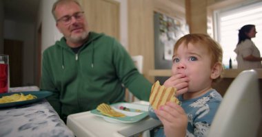 Bebek kahvaltıda yüksek sandalyede otururken waffle yiyor, baba sıcak bir ilişki kuruyor ve sıcak bir ev mutfağı kuruyor.