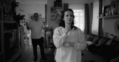 Kadın hararetli tartışmalar sırasında derin düşüncelere dalarken, arka plandaki erkek hayal kırıklığı, gerginlik ve bir çiftin ilişkilerindeki çözülmemiş sorunları işaret ediyor.