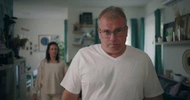 Erkek, tartışma sırasında yoğun bir ifadeyle kameraya bakıyor, kadın oturma odasında, gergin ve duygusal bir ilişki çatışması ve hüsran anı yaşıyor.