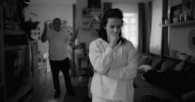 Kadın hararetli tartışmalar sırasında derin düşüncelere dalarken, arka plandaki erkek hayal kırıklığı, gerginlik ve bir çiftin ilişkilerindeki çözülmemiş sorunları işaret ediyor.