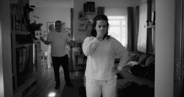 Kadın hararetli tartışmalar sırasında kafasını tutarken, arka plandaki erkek öfkeyle işaret ediyor, bir çiftin ilişkilerinde yoğun bir çatışma ve duygusal sıkıntı yakalıyor.