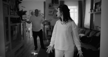 Kadın hararetli tartışmalar sırasında kafasını tutarken, arka plandaki erkek öfkeyle işaret ediyor, bir çiftin ilişkilerinde yoğun bir çatışma ve duygusal sıkıntı yakalıyor.